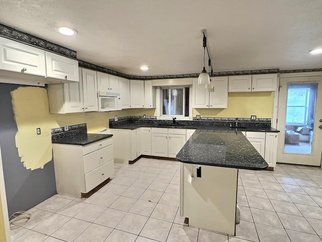 kitchen featuring a sink, white cabinetry, a peninsula, light tile patterned floors, and white microwave