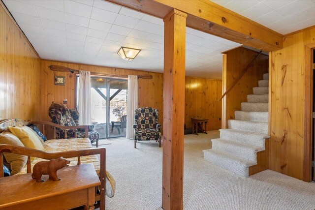 carpeted living room with wooden walls and stairway