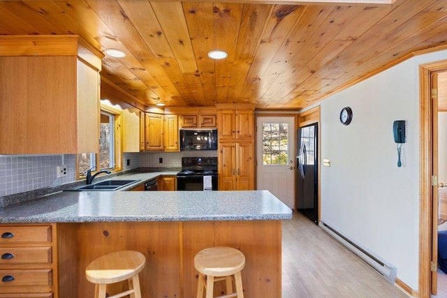 kitchen featuring tasteful backsplash, a baseboard heating unit, a peninsula, black appliances, and a sink