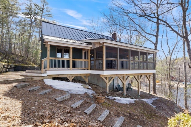 back of house featuring a standing seam roof, a sunroom, a chimney, and metal roof