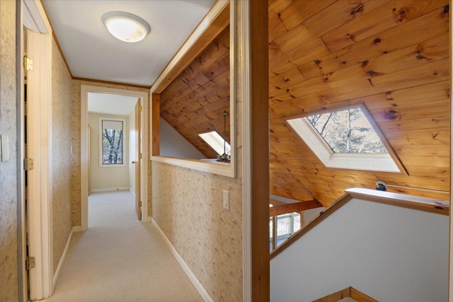corridor with carpet floors, an upstairs landing, wallpapered walls, baseboards, and lofted ceiling with skylight