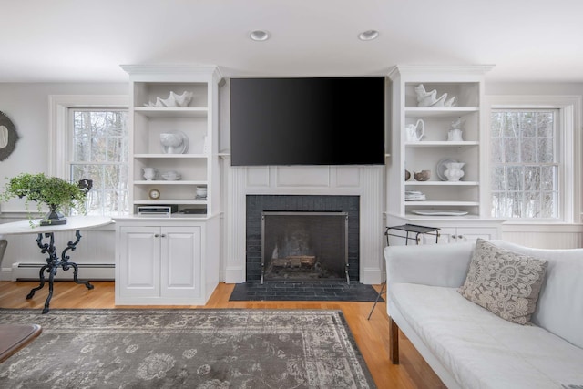 72 Natures Way, Wells, ME 04090 - living room with a baseboard heating unit, wood finished floors, a fireplace with flush hearth, plenty of natural light, and recessed lighting