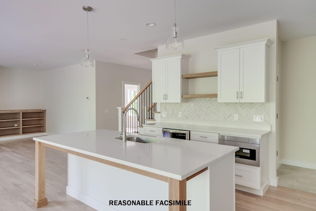 kitchen with light wood finished floors, tasteful backsplash, an island with sink, a sink, and open shelves
