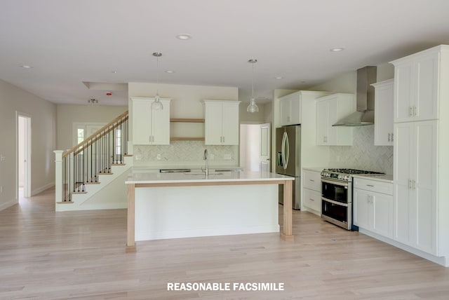 kitchen with light countertops, white cabinets, a kitchen island with sink, appliances with stainless steel finishes, and wall chimney exhaust hood