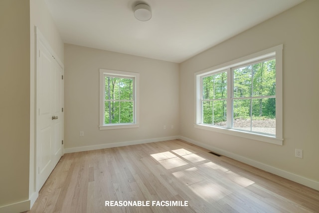 empty room with light wood-type flooring, plenty of natural light, baseboards, and visible vents