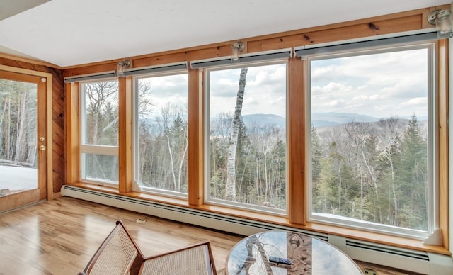 sunroom featuring a wooded view, a mountain view, a baseboard heating unit, and wood finished floors