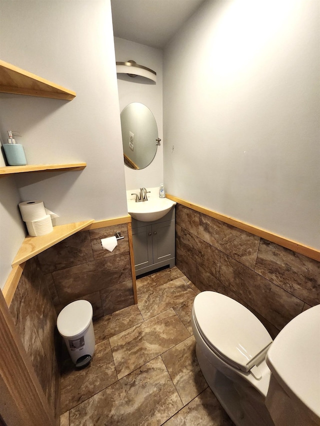 bathroom with toilet, a wainscoted wall, tile walls, and vanity