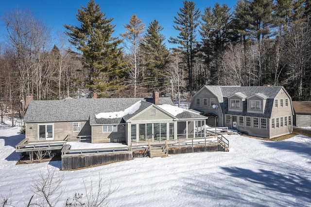snow covered property with a deck, a gambrel roof, and a sunroom