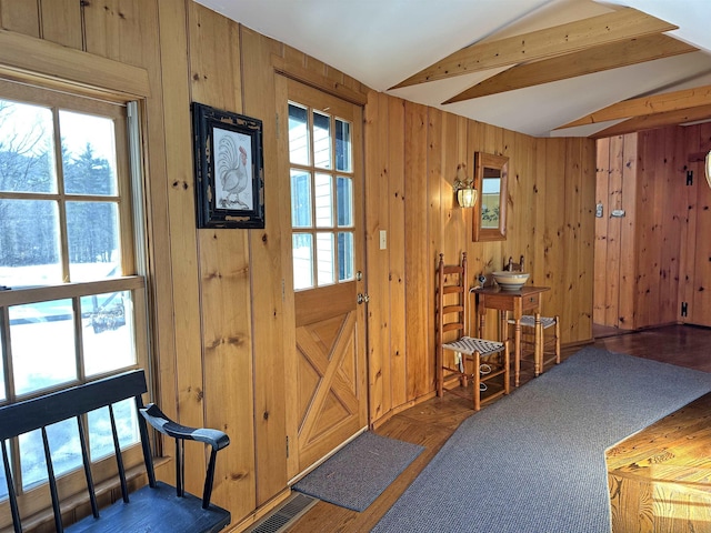 entrance foyer featuring wood walls, lofted ceiling with beams, and plenty of natural light