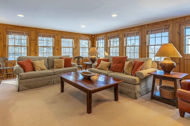 living area with light carpet, plenty of natural light, and wooden walls