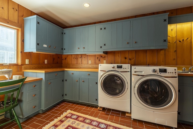 laundry area with brick patterned floor, separate washer and dryer, a sink, wooden walls, and cabinet space