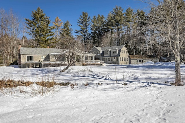 snow covered rear of property featuring a gambrel roof and a sunroom