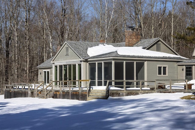 snow covered property with a sunroom, a chimney, a shingled roof, and a deck