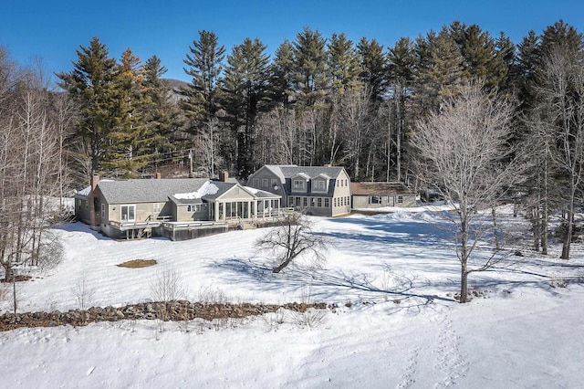 snow covered rear of property with a view of trees and a sunroom