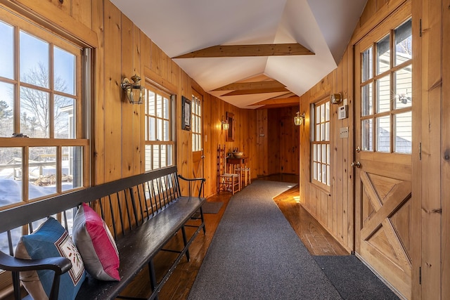 corridor with dark carpet, wood walls, and lofted ceiling with beams