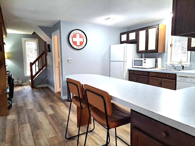 kitchen with white appliances, light countertops, a breakfast bar area, a sink, and wood finished floors