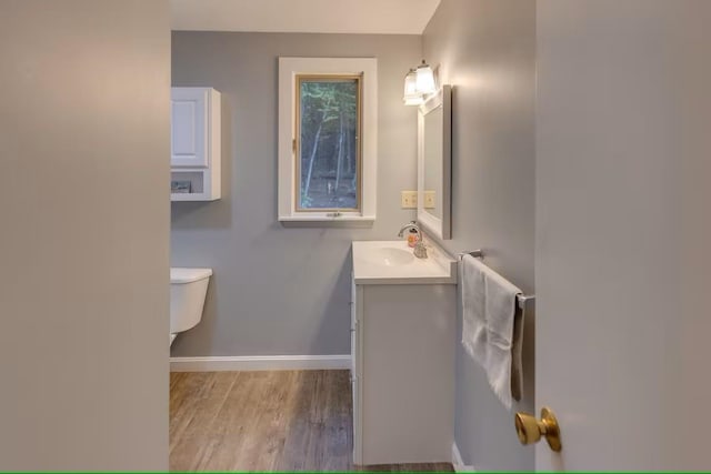 half bath featuring toilet, baseboards, vanity, and wood finished floors
