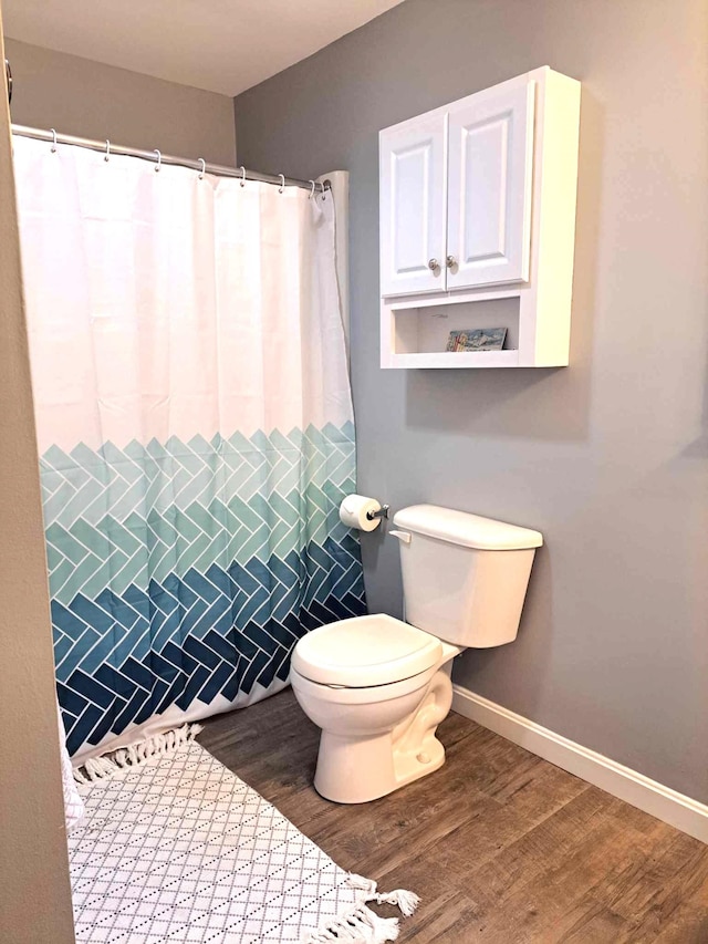 bathroom featuring curtained shower, baseboards, toilet, and wood finished floors