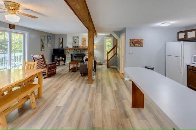 dining space featuring beamed ceiling, a stone fireplace, stairway, and light wood-style floors