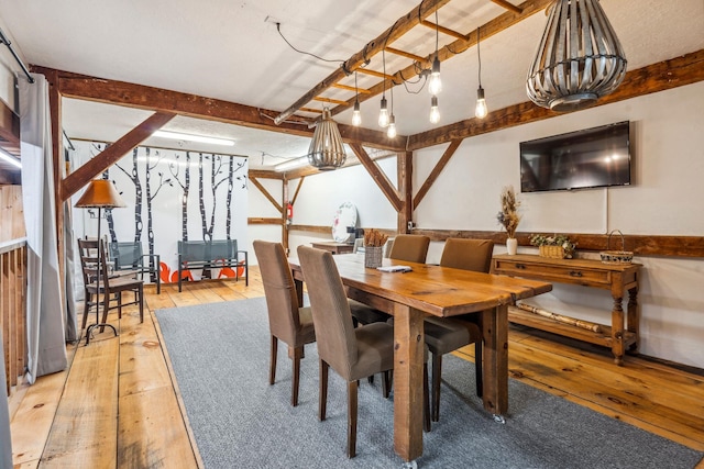 dining area featuring light wood finished floors and beamed ceiling