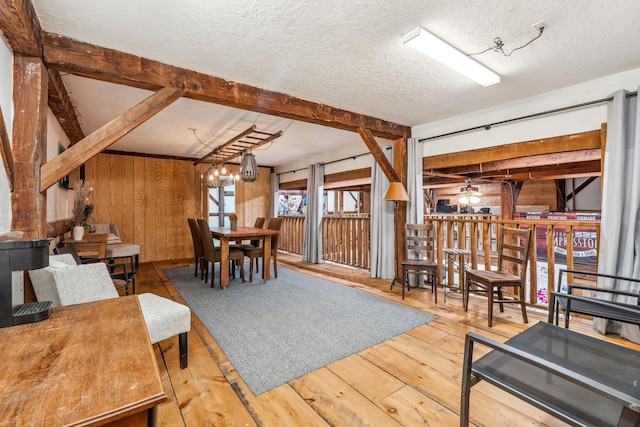 dining area with a textured ceiling, wood walls, wood-type flooring, and beam ceiling