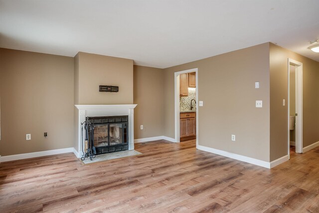 114 Winterwood Dr Unit 114, Londonderry, NH 03053 - unfurnished living room with light wood-style flooring, a sink, a fireplace with flush hearth, and baseboards