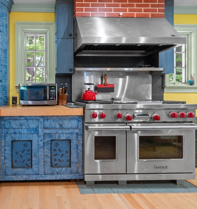 kitchen with exhaust hood, ornamental molding, appliances with stainless steel finishes, wood finished floors, and backsplash