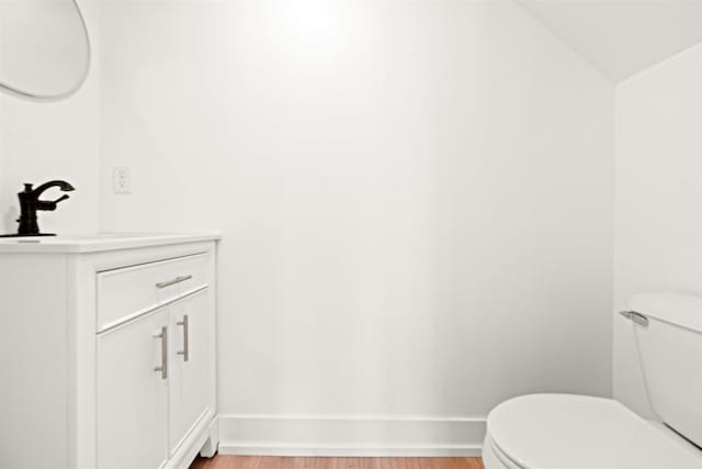 half bath with toilet, wood finished floors, and baseboards