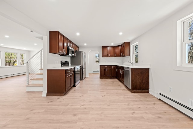kitchen featuring arched walkways, a baseboard radiator, light wood finished floors, stainless steel appliances, and a baseboard heating unit