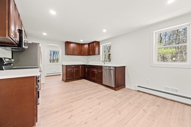 kitchen featuring light wood-type flooring, light countertops, appliances with stainless steel finishes, arched walkways, and a baseboard radiator