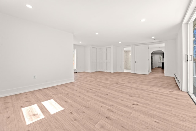 unfurnished living room with recessed lighting, arched walkways, a baseboard heating unit, and light wood-style floors