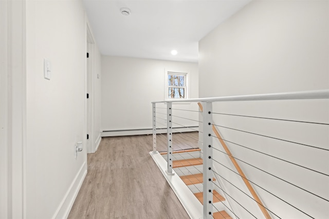 hallway with an upstairs landing, light wood-style flooring, and a baseboard heating unit