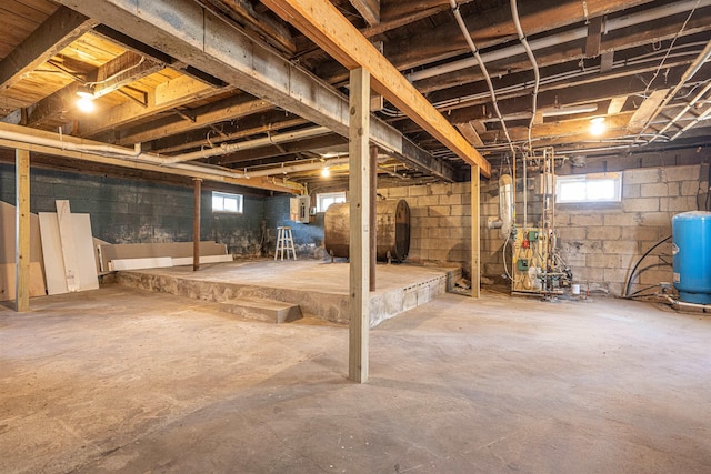 basement featuring electric panel, heating fuel, a heating unit, and concrete block wall