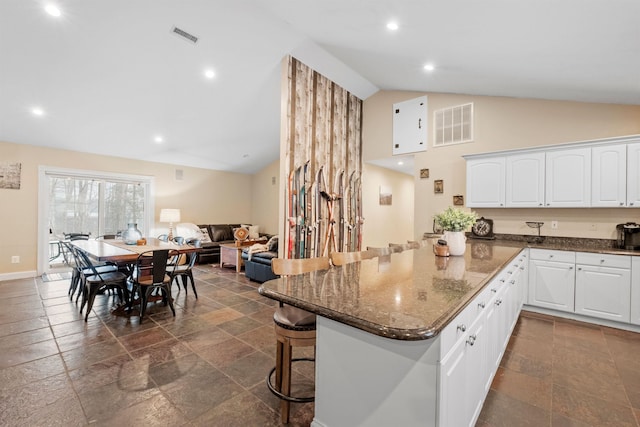 kitchen featuring visible vents, white cabinets, open floor plan, a kitchen breakfast bar, and dark stone counters