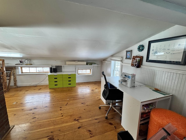 unfurnished office with light wood-style floors, a wall unit AC, wainscoting, and lofted ceiling
