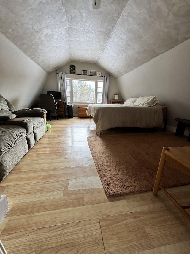 bedroom with light wood-style flooring, a textured ceiling, and lofted ceiling