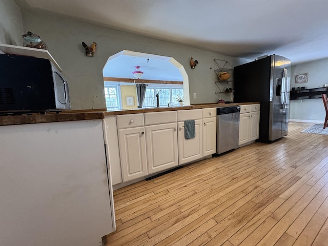 kitchen featuring light wood-style flooring, white cabinets, stainless steel appliances, arched walkways, and a sink