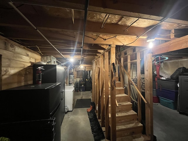 unfinished basement featuring strapped water heater, freestanding refrigerator, stairway, and washer / dryer
