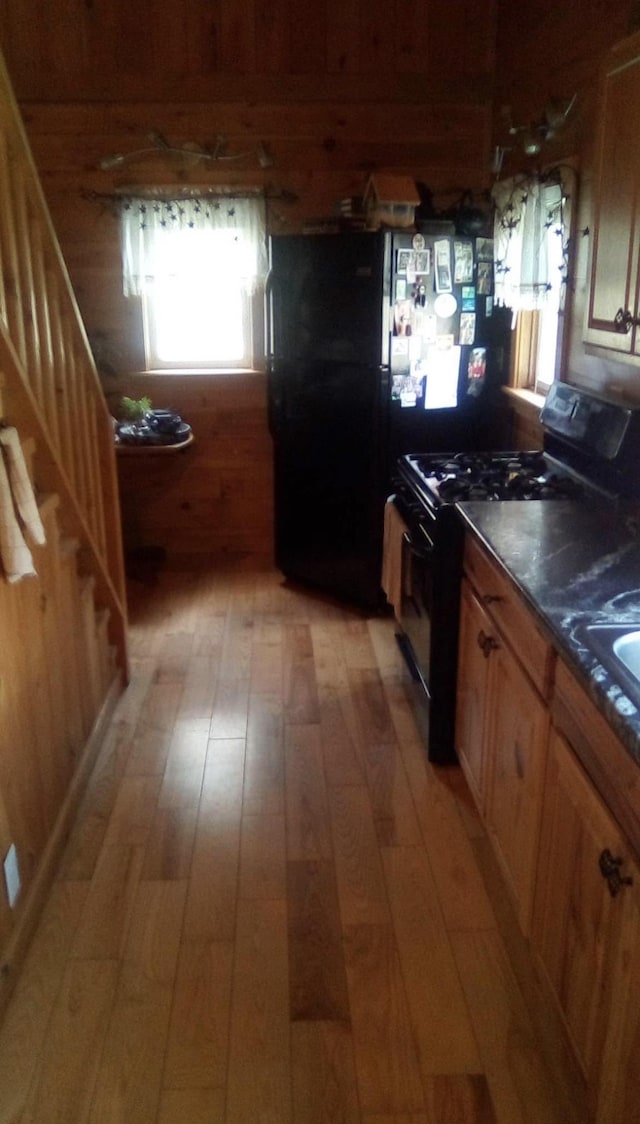 kitchen with light wood-style floors, brown cabinetry, black appliances, wood walls, and dark countertops