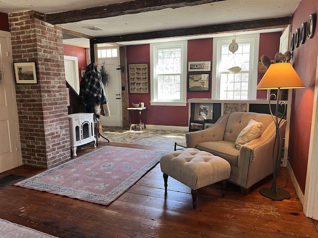living room featuring a wood stove, hardwood / wood-style flooring, baseboards, and beam ceiling