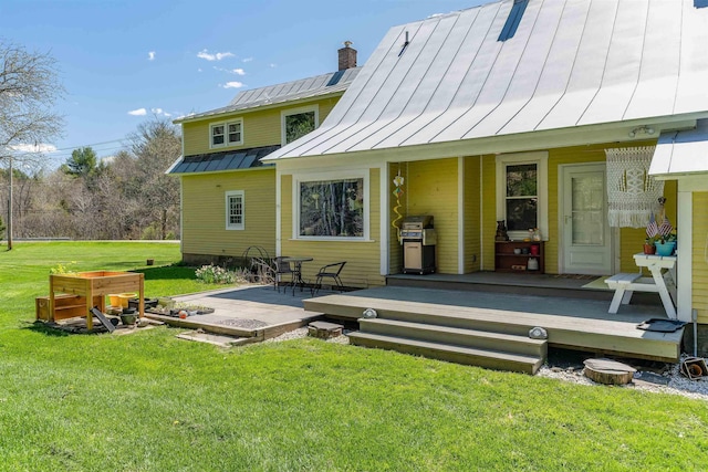rear view of house featuring a yard, a standing seam roof, metal roof, and a chimney