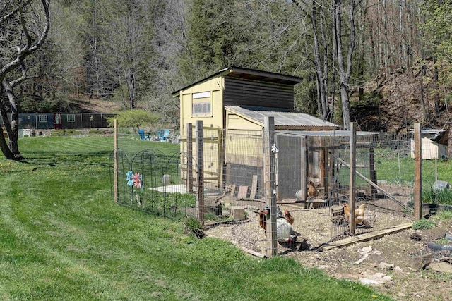 view of poultry coop featuring a forest view, fence, and a lawn