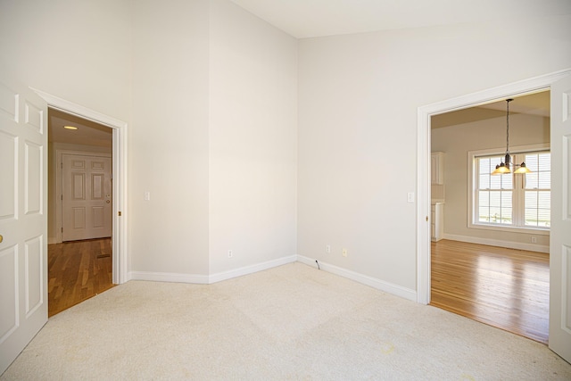 spare room with baseboards, carpet floors, wood finished floors, and a high ceiling