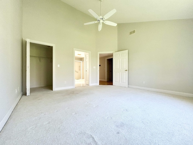 unfurnished bedroom featuring high vaulted ceiling, light carpet, baseboards, a walk in closet, and connected bathroom