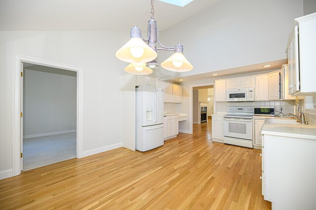 kitchen with white appliances, a sink, a skylight, light wood-style flooring, and baseboards