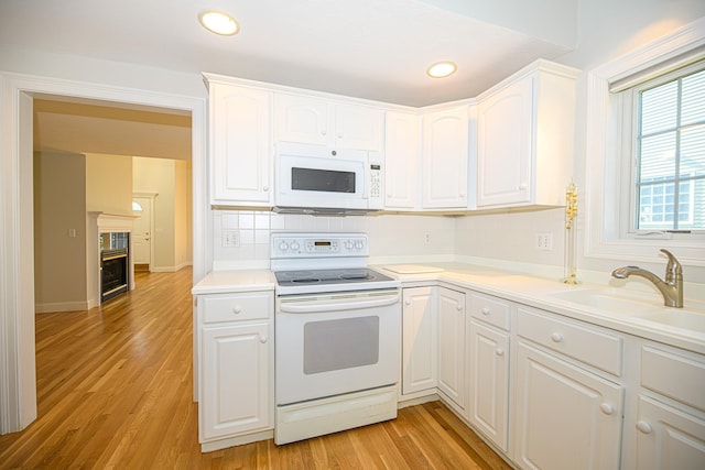 kitchen featuring white appliances, light wood-style flooring, white cabinetry, decorative backsplash, and a sink