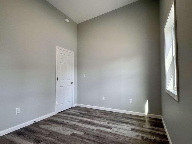 empty room with dark wood-type flooring, baseboards, and lofted ceiling