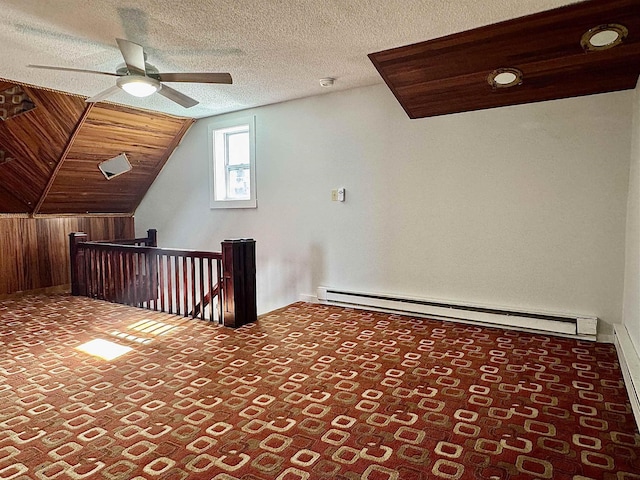 additional living space featuring a baseboard radiator, ceiling fan, a textured ceiling, vaulted ceiling, and wood walls