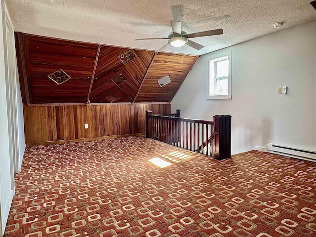 additional living space with baseboards, ceiling fan, a textured ceiling, wood walls, and a baseboard heating unit