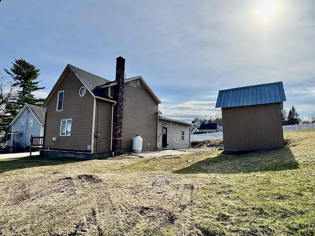 view of side of property featuring a lawn, a storage shed, a chimney, and an outbuilding